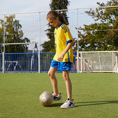 A girl in a soccer uniform plays football at a sports arena.